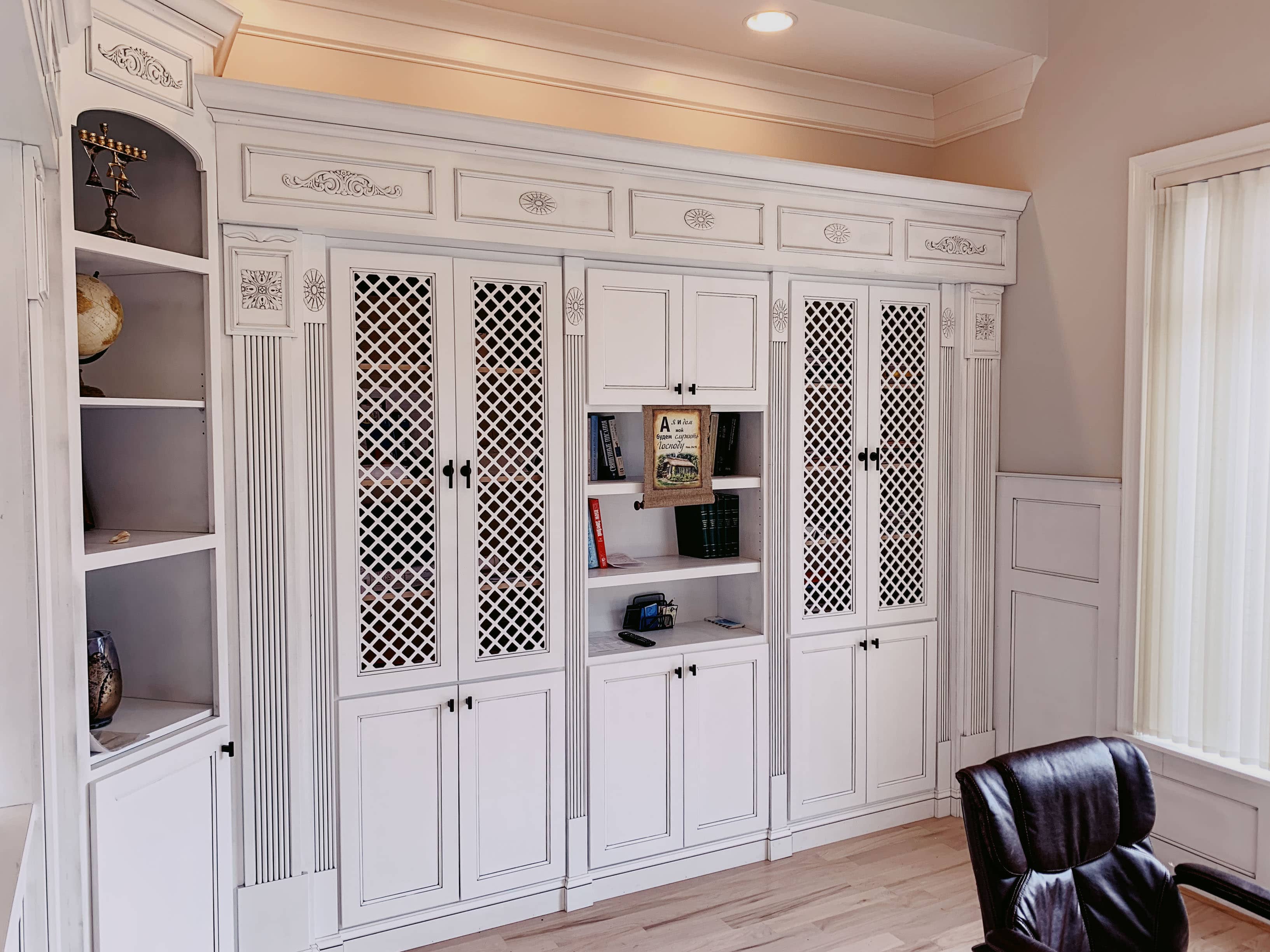 Custom white built-in armoire with glass doors and ornate millwork detail by GM Cabinetry