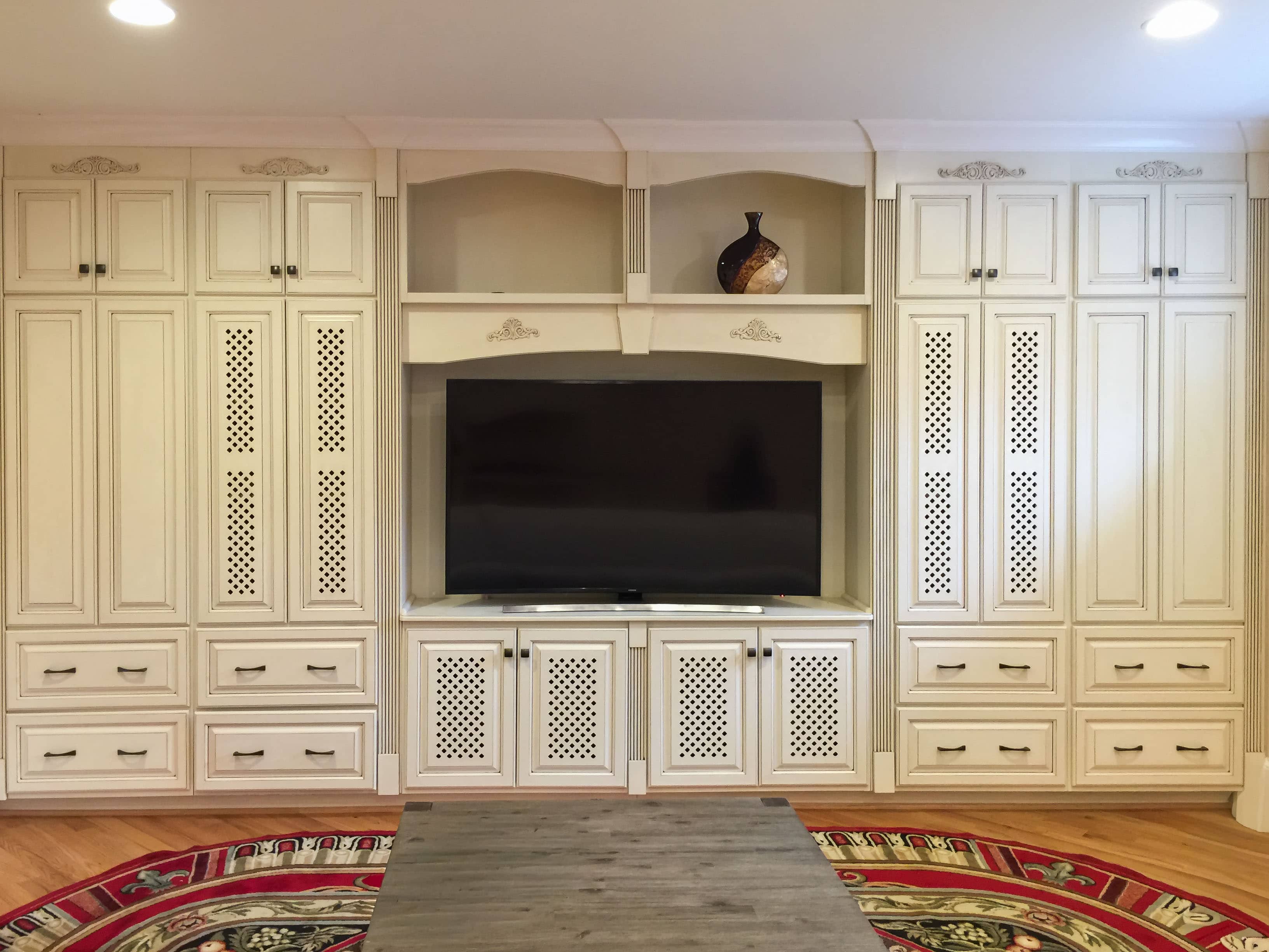 Custom built-in entertainment center with ornate cream cabinetry and recessed TV niche by GM Cabinetry