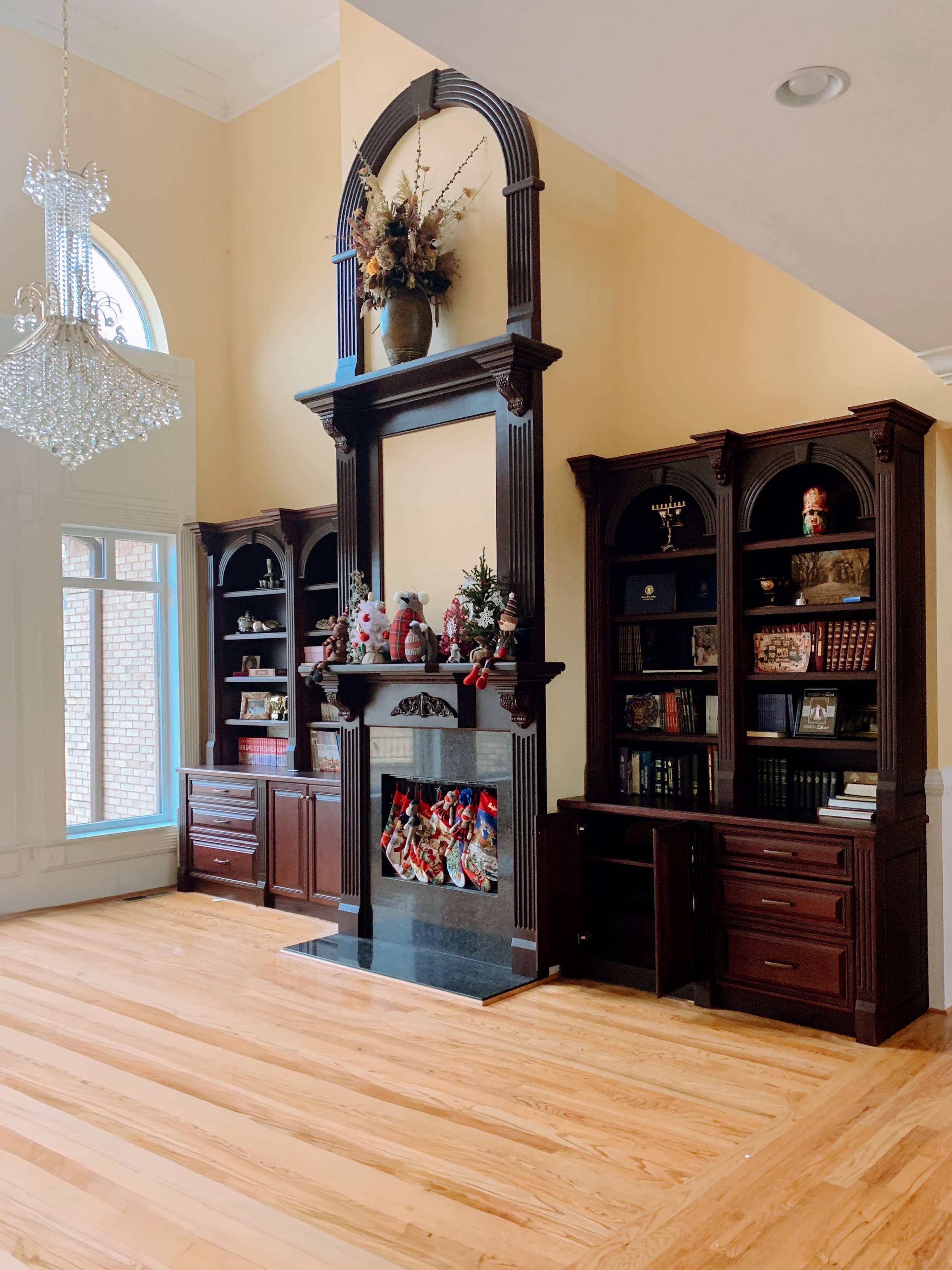 Dark wood built-in media center with fireplace surround, bookshelves, and chandelier in formal living room