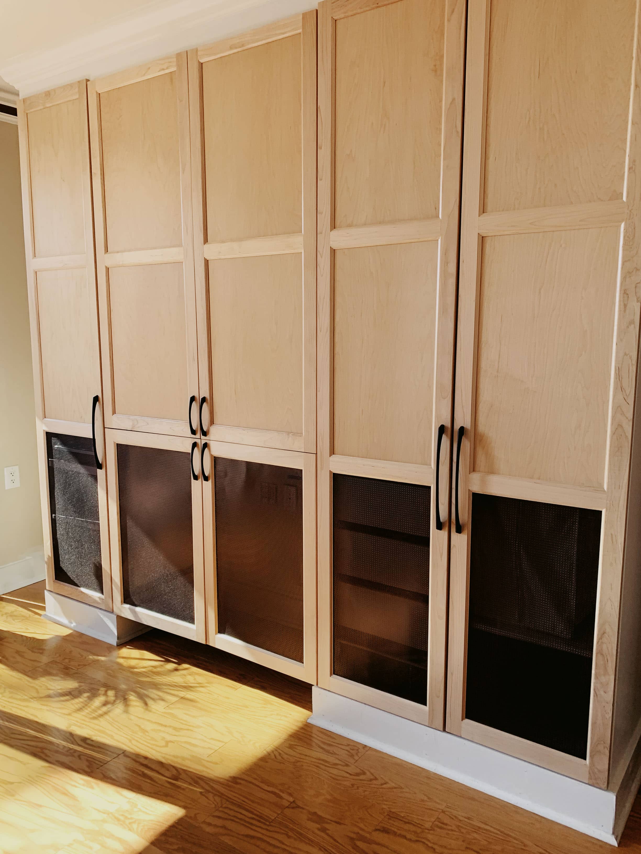 Floor-to-ceiling natural maple media cabinets with perforated mesh ventilation panels