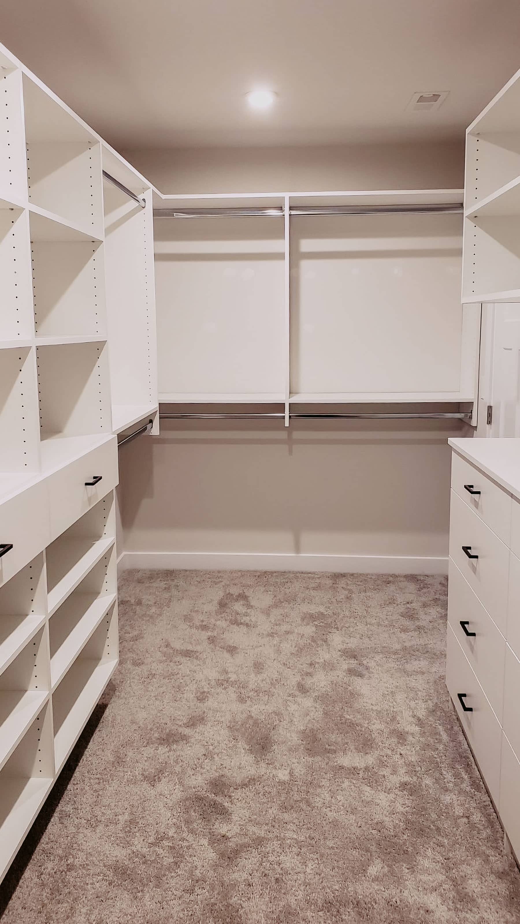 Custom walk-in closet with white built-in shelving, drawers, and hanging rods by GM Cabinetry in Georgia