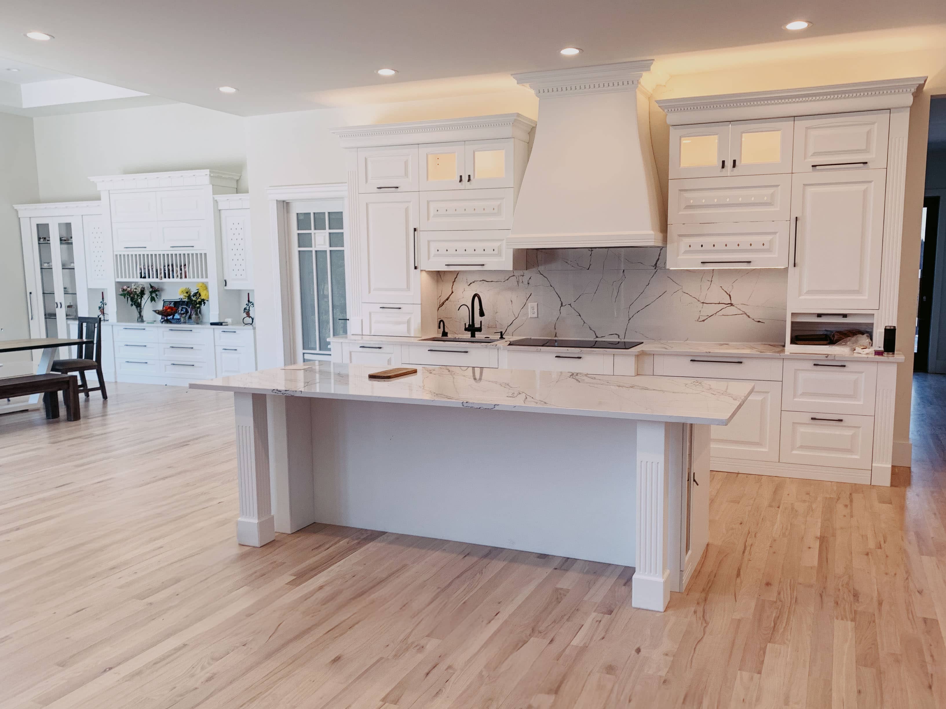 Grand white kitchen with custom range hood, marble backsplash, and large center island by GM Cabinetry