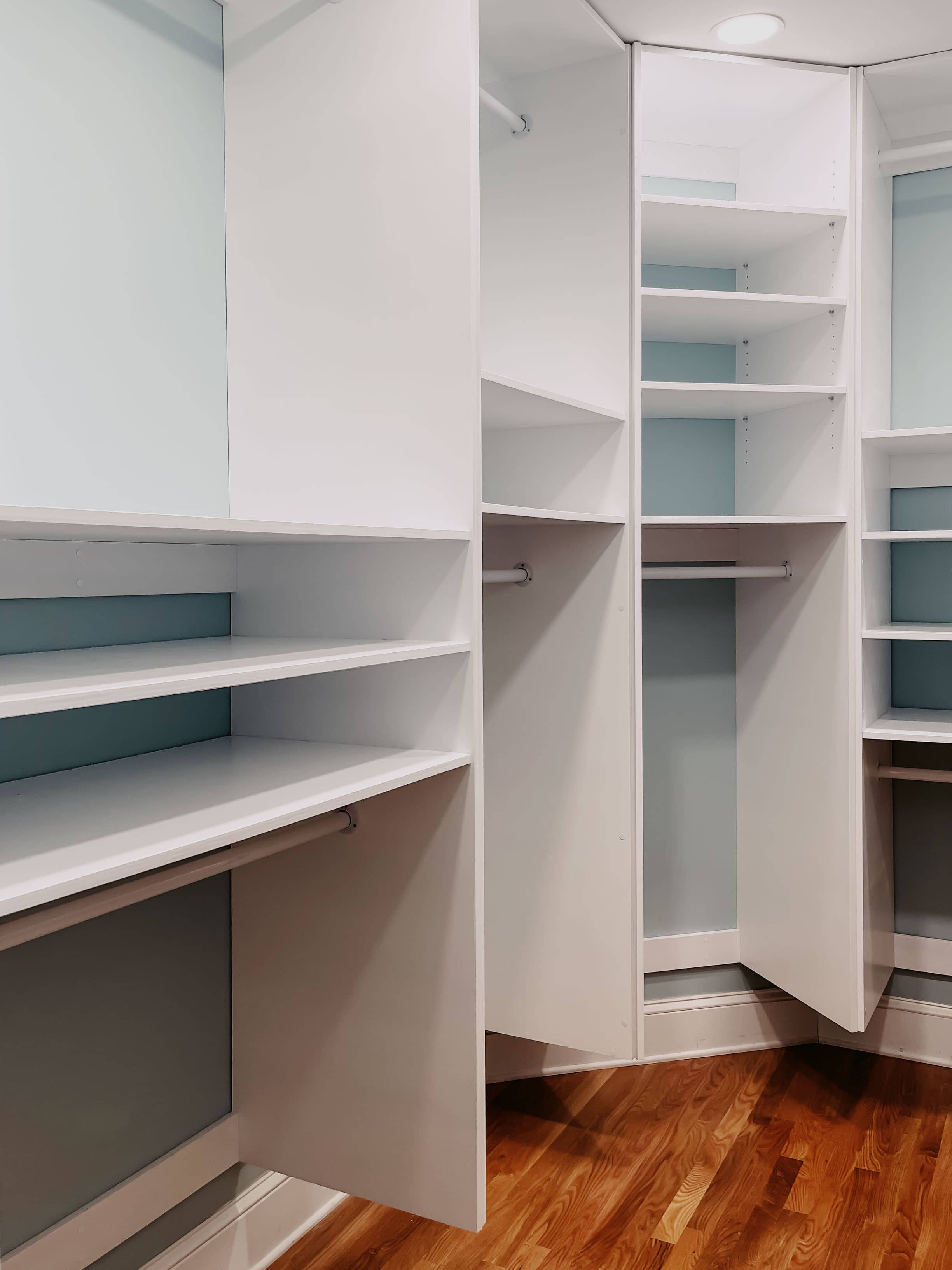 Completed walk-in closet with custom white shelving, adjustable rods, and drawer storage by GM Cabinetry