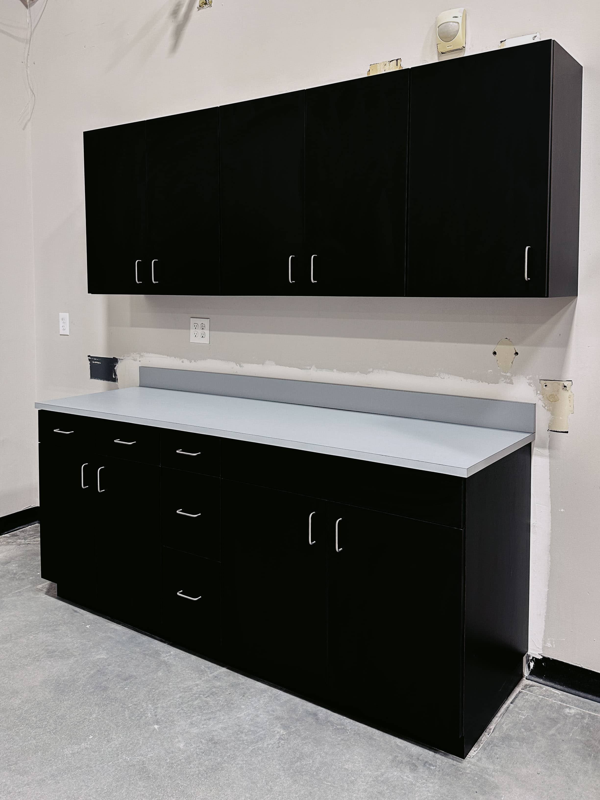 Black commercial-grade upper and lower cabinets with grey laminate counter installed in office break room