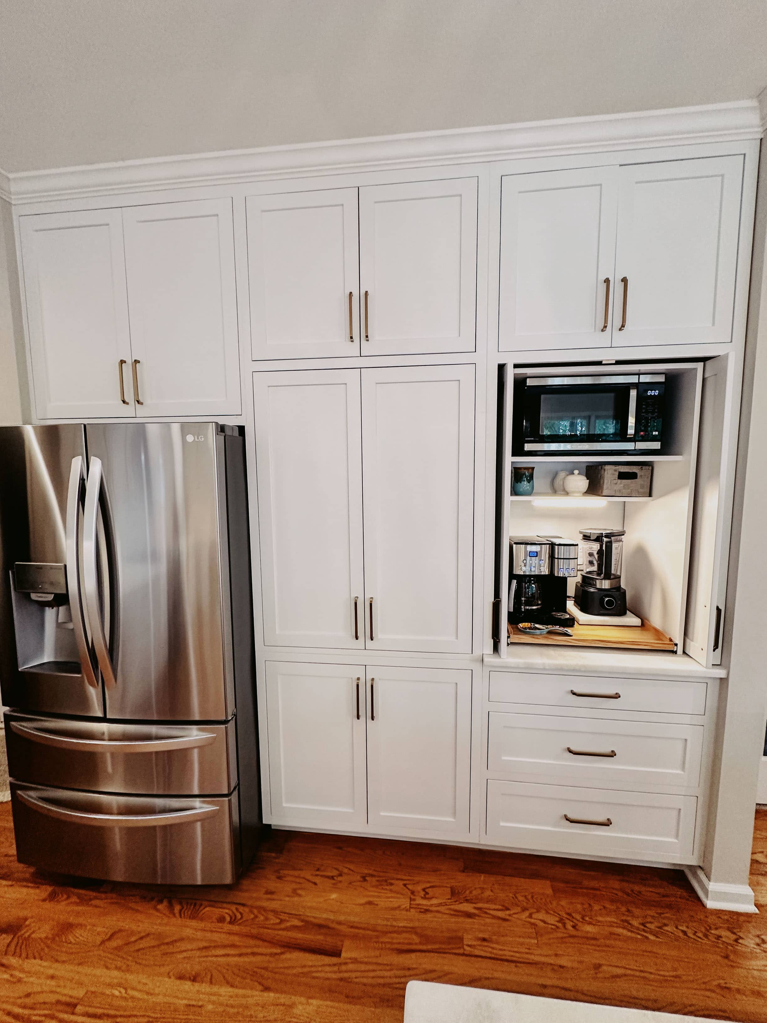 Floor-to-ceiling white pantry cabinets with hidden coffee station, microwave niche, and pocket doors by GM Cabinetry